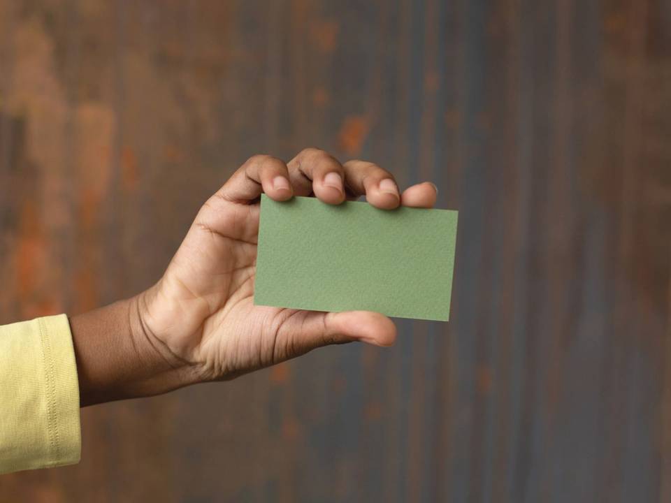 A hand holds a blank sage-green business card against a rust-brown background.